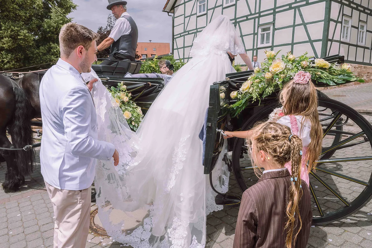 Der Bräutigam hilft der Braut mit dem langen Schleier, beim einsteigen in die Hochzeitskutsche
