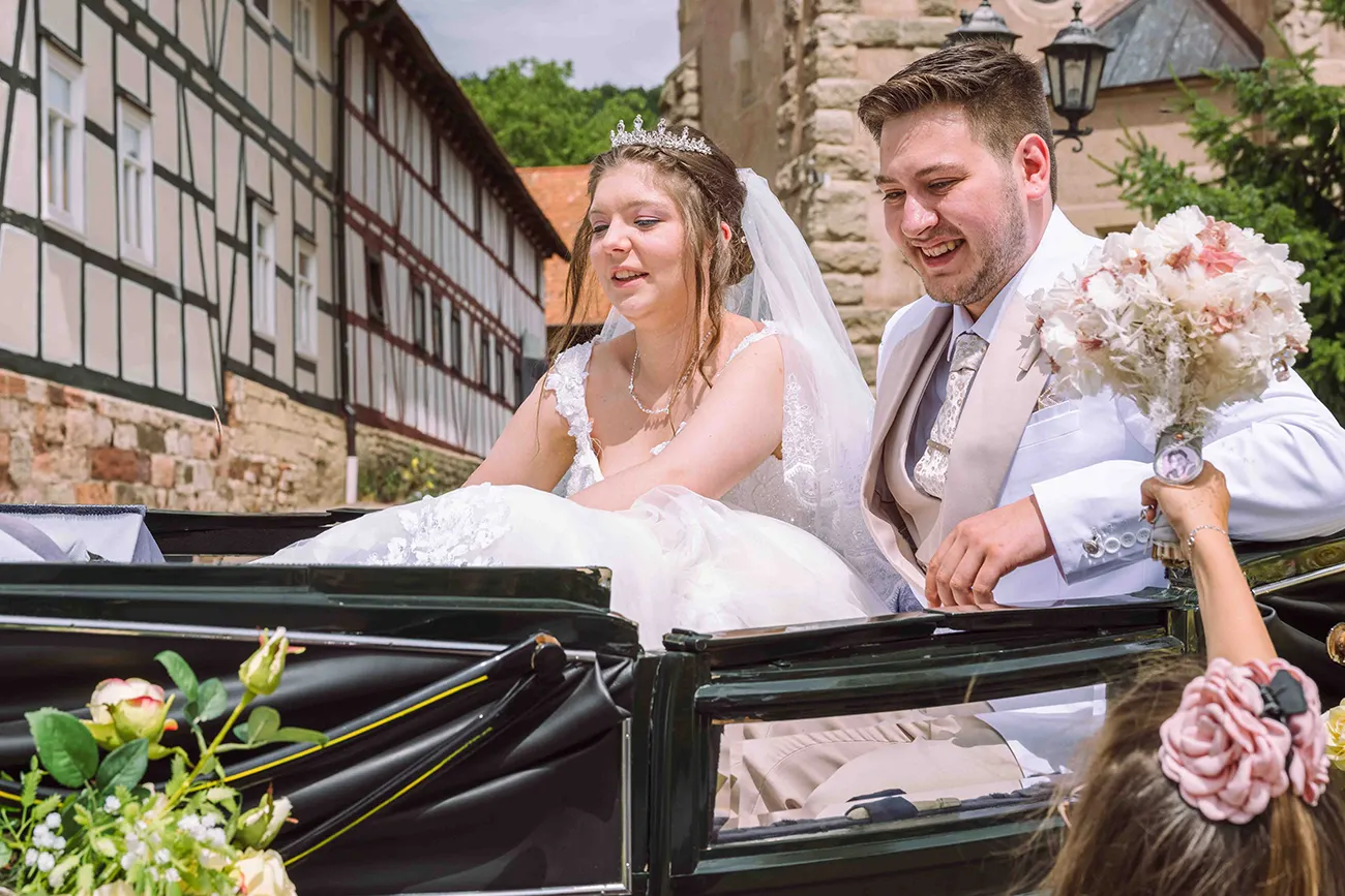Dem Brautpaar wird vom Blumenmädchen der Brautstrauß in die Kutsche gereicht
