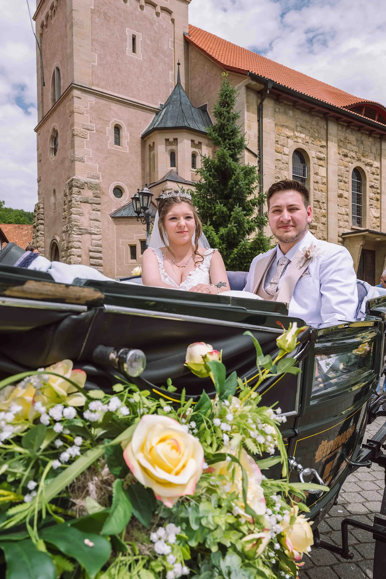Brautpaar sitzt in mit Blumen verzierten Hochzeitskutsche
