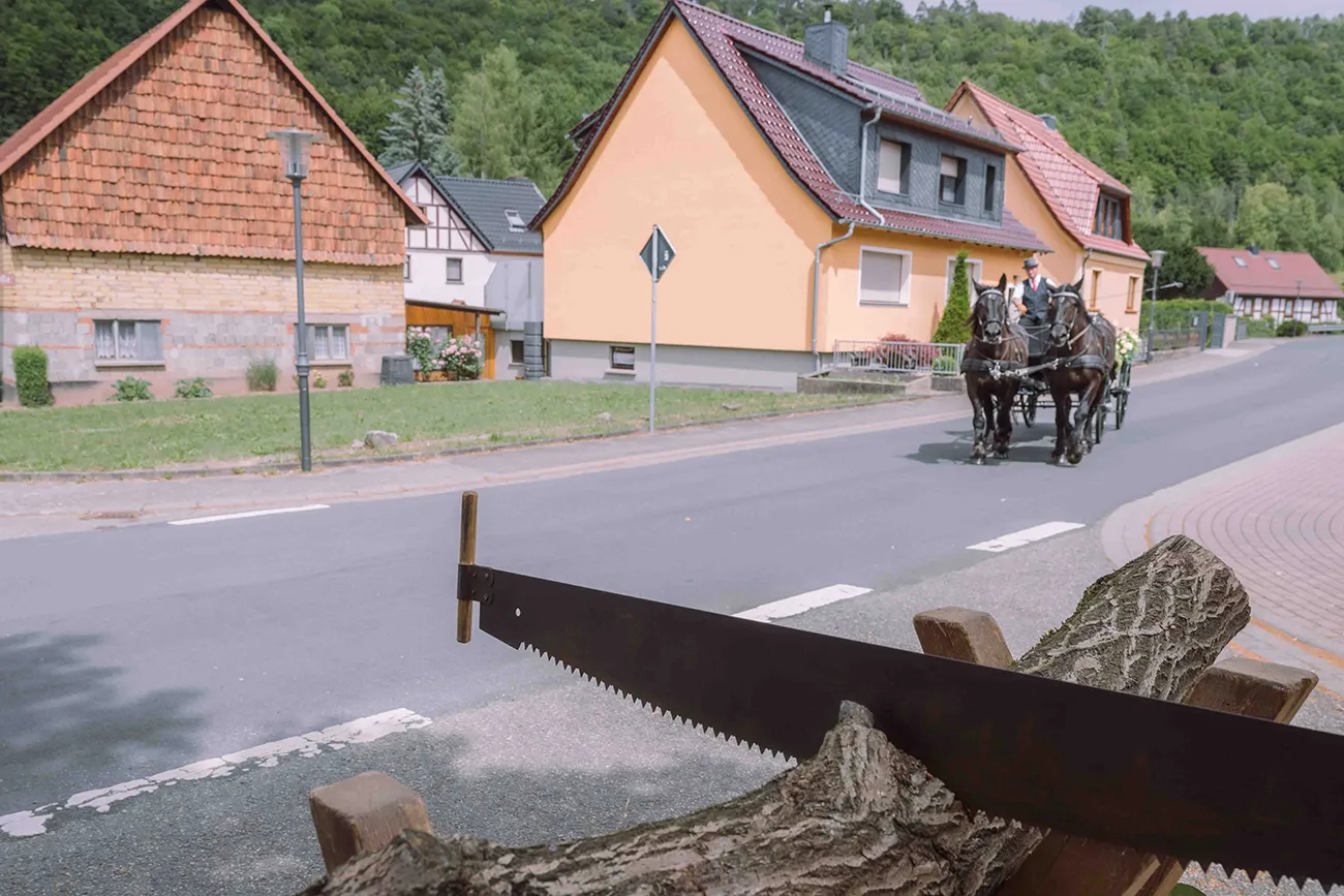 Hochzeitsreportage der Sägebock mit Baumstamm und die Hochzeitskutsche im Hintergrund