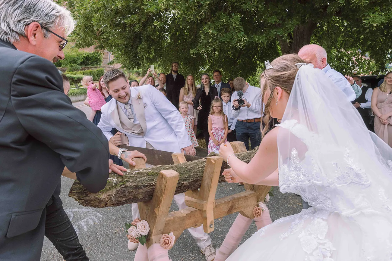 Hochzeitsfotografie, das Brautpaar beim durchsägen eines Baumstamm