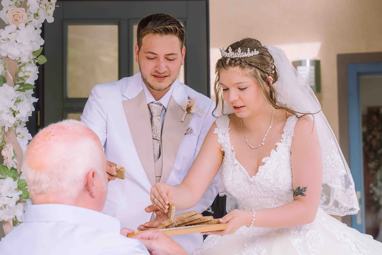 Hochzeitsreportage, dem Hochzeitspaar wird Brot und Salz gereicht. Ein altes Hochzeits- Ritual