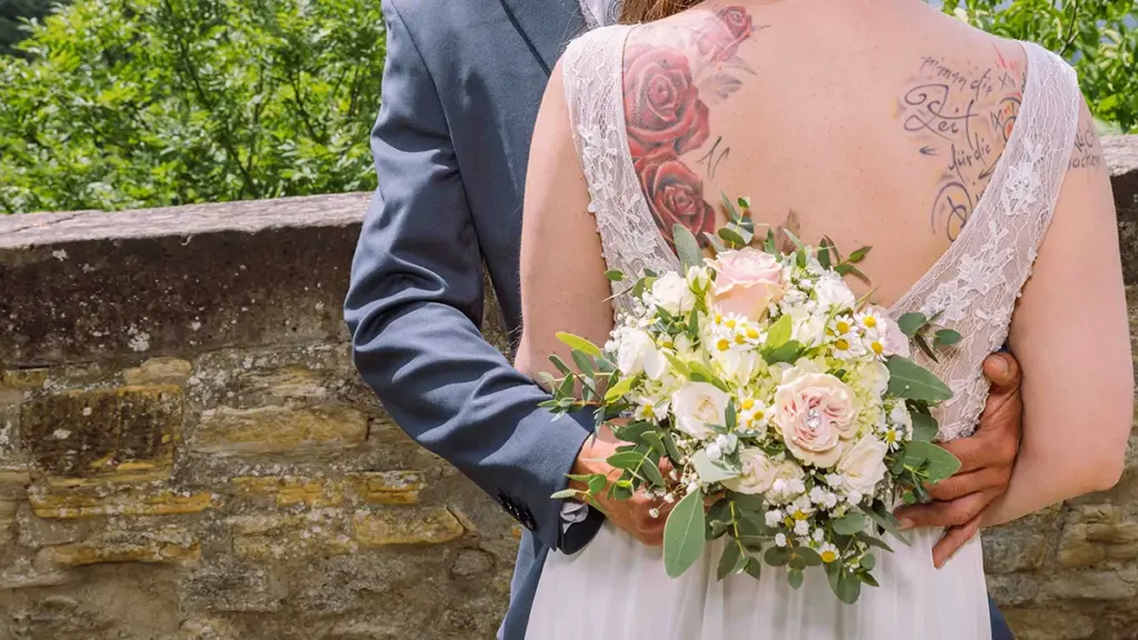 Braut und Bräutigam umarmen sich beim Brautpaarshooting auf der Hochzeit. Rückenansicht der Braut mit tätowierten Rücken.
