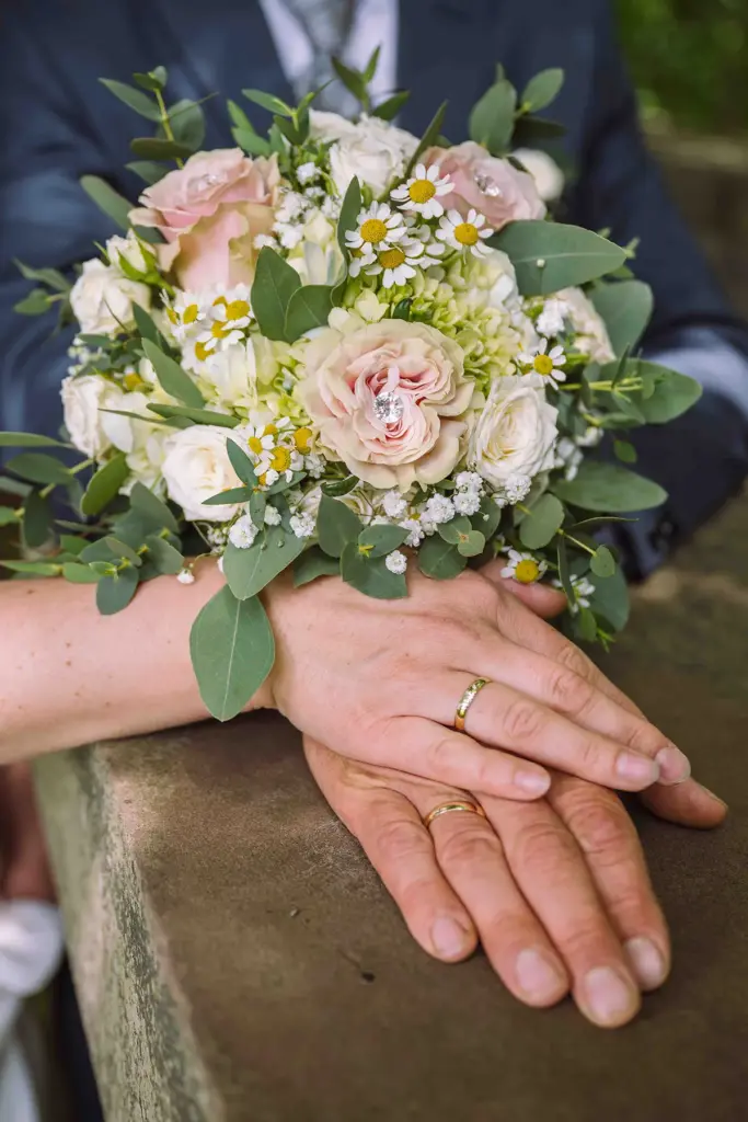 Brautstrauß mit gekreuzten Händen des Brautpaar mit Eheringen