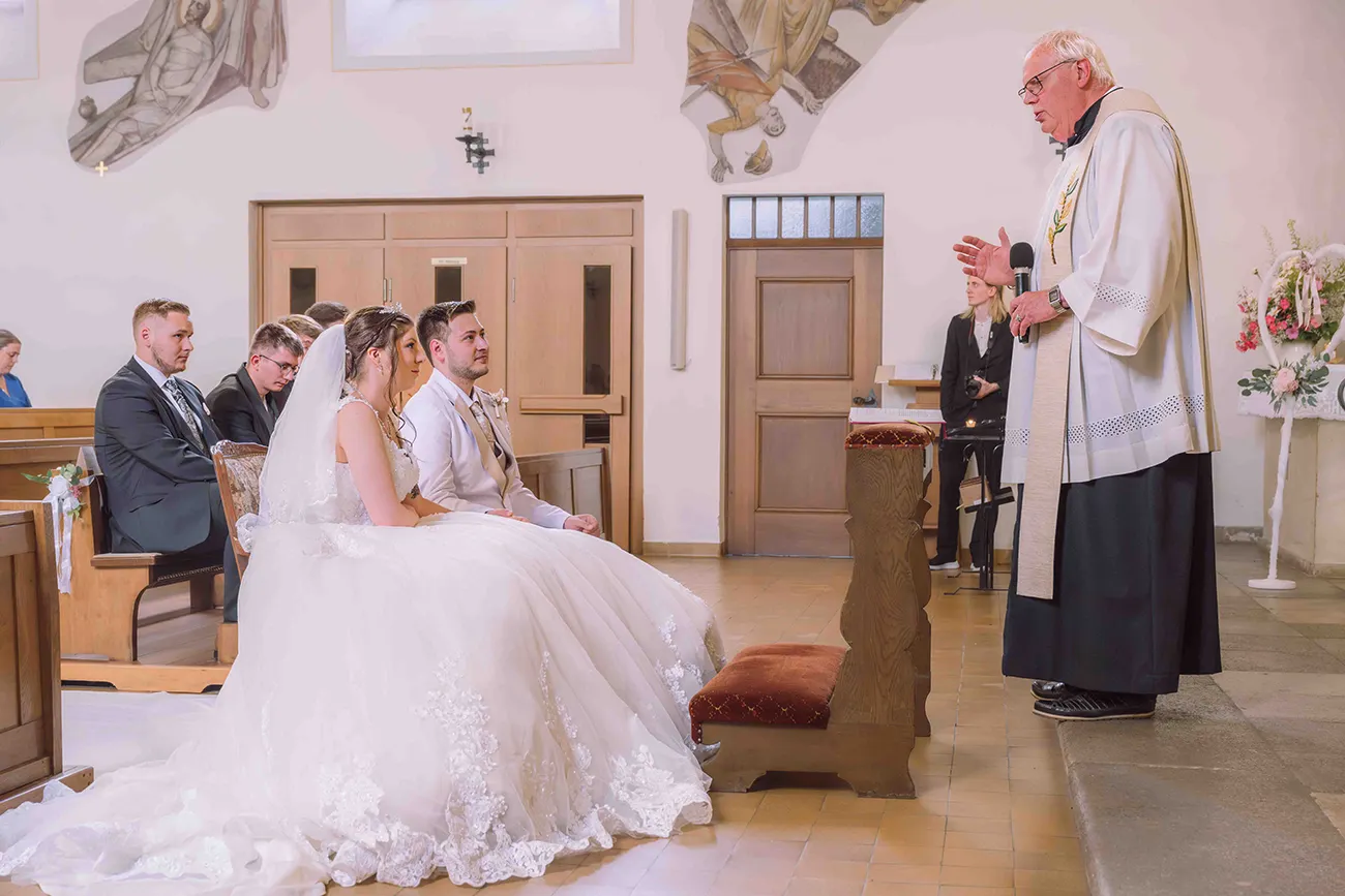 Brautpaar bei der kirchlichen Trauung mit Pastor, seitlich fotografiert. Hochzeitsreportage