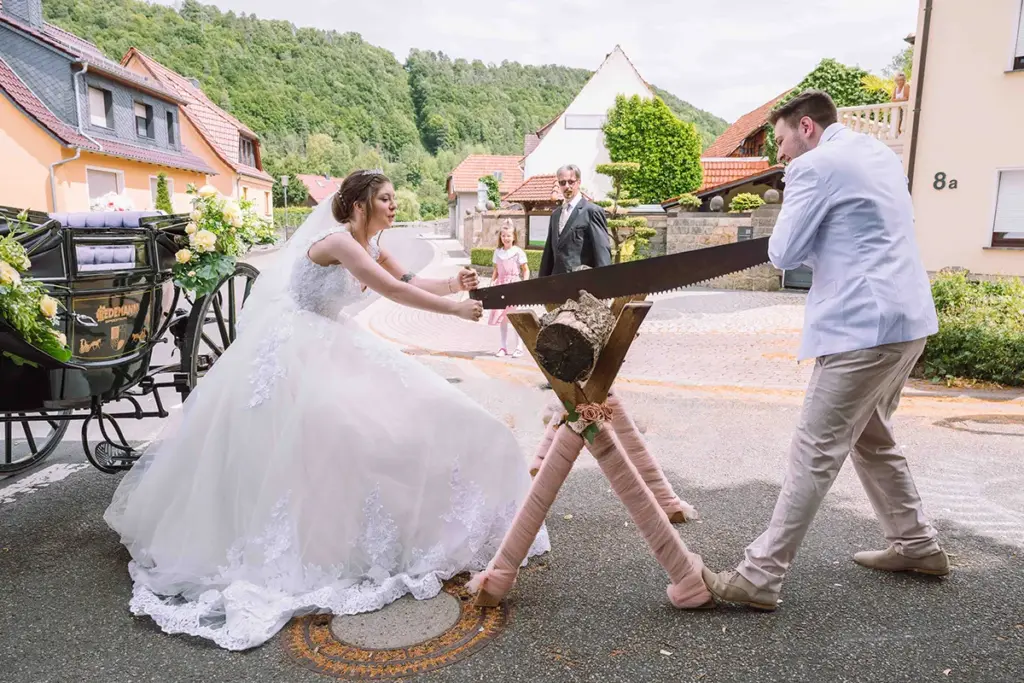 Hochzeitsreportage, das Brautpaar sägt gemeinsam einen Baumstamm durch, ein alter Hochzeitsbrauch