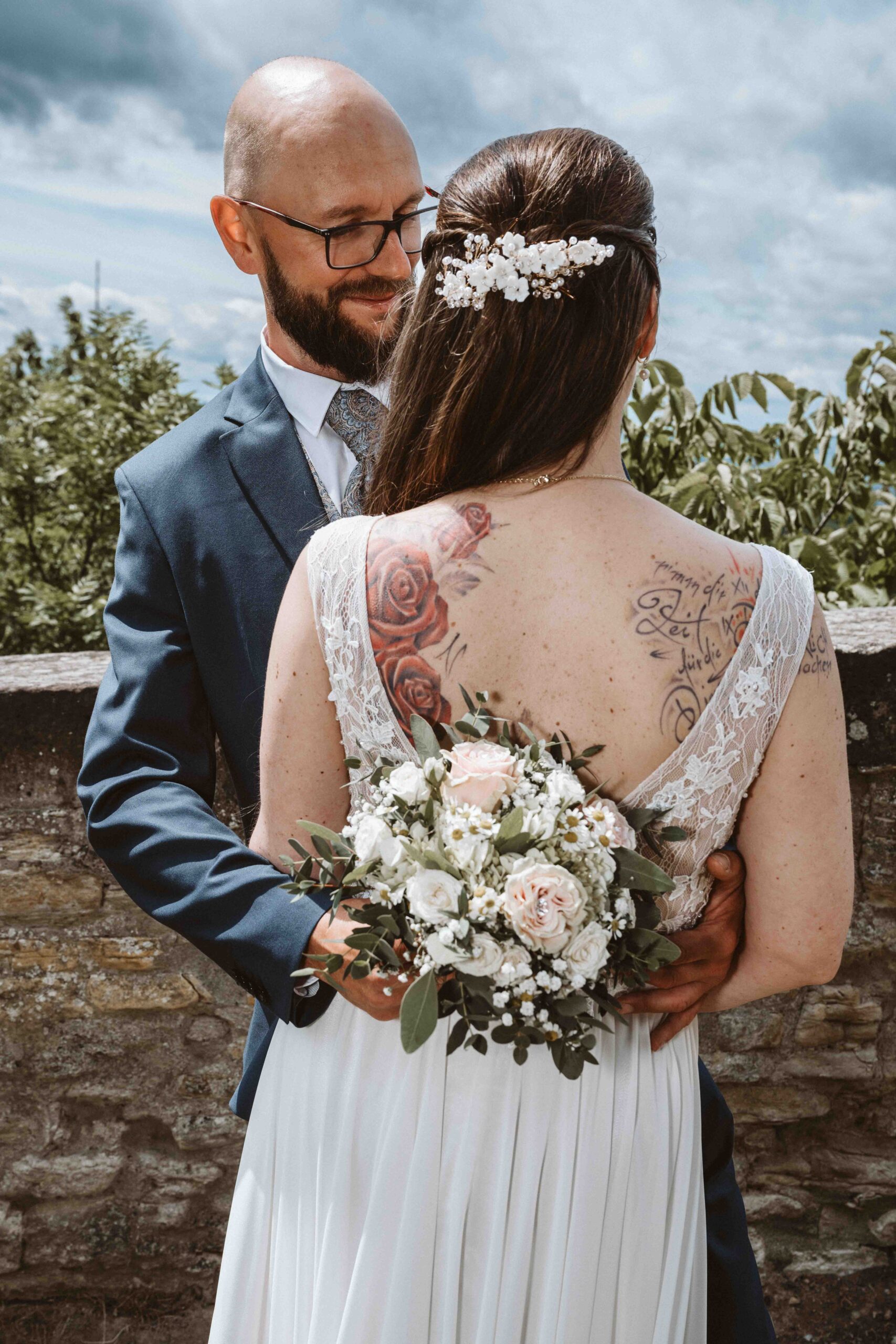 Brautpaarshooting bei der Hochzeit. Bräutigam hält Braut im Arm, Rückenansicht der Braut mit Brautstrauß