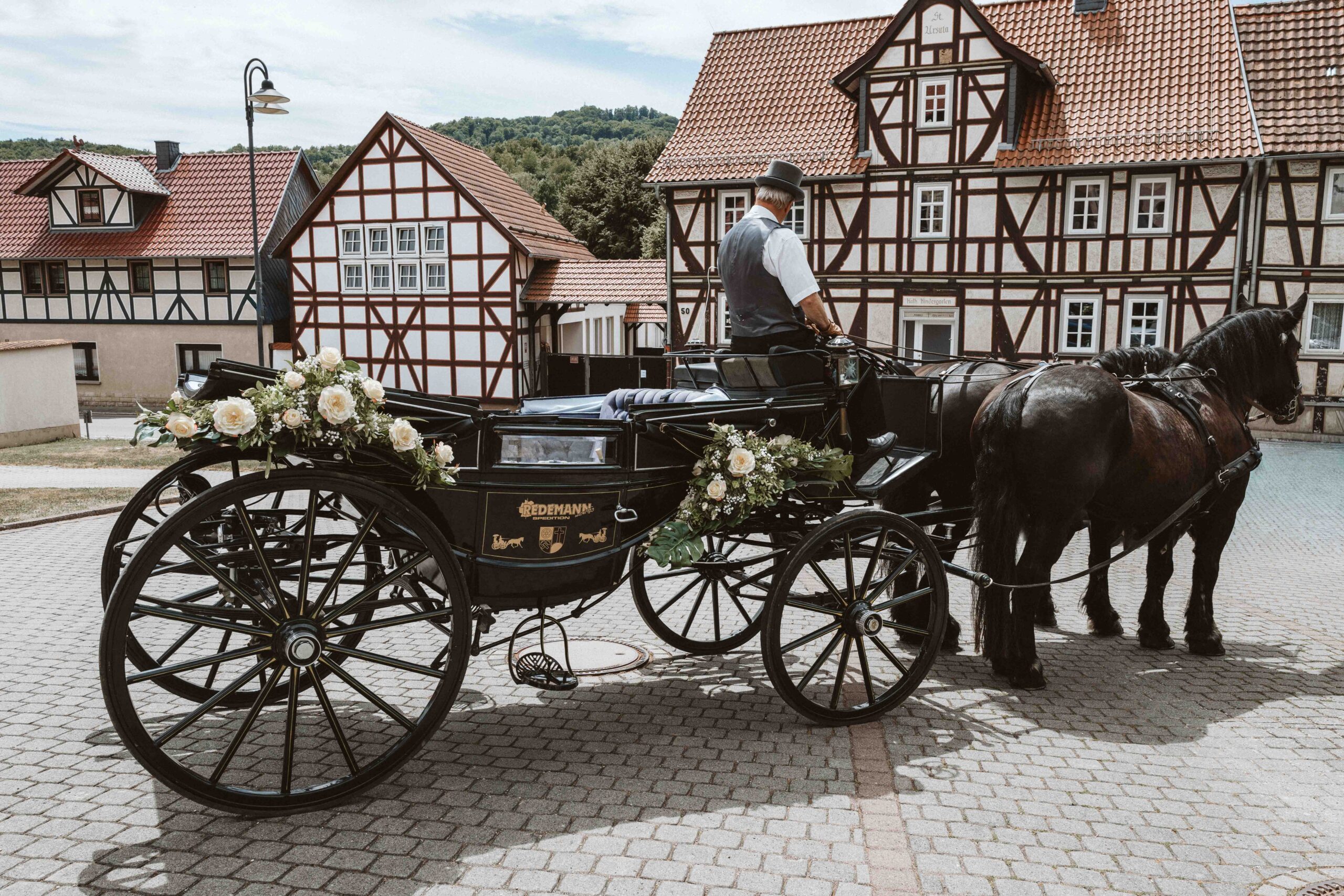Der Kutscher wartet mit der mit Rosen geschmückten Hochzeitskutsche auf das Brautpaar