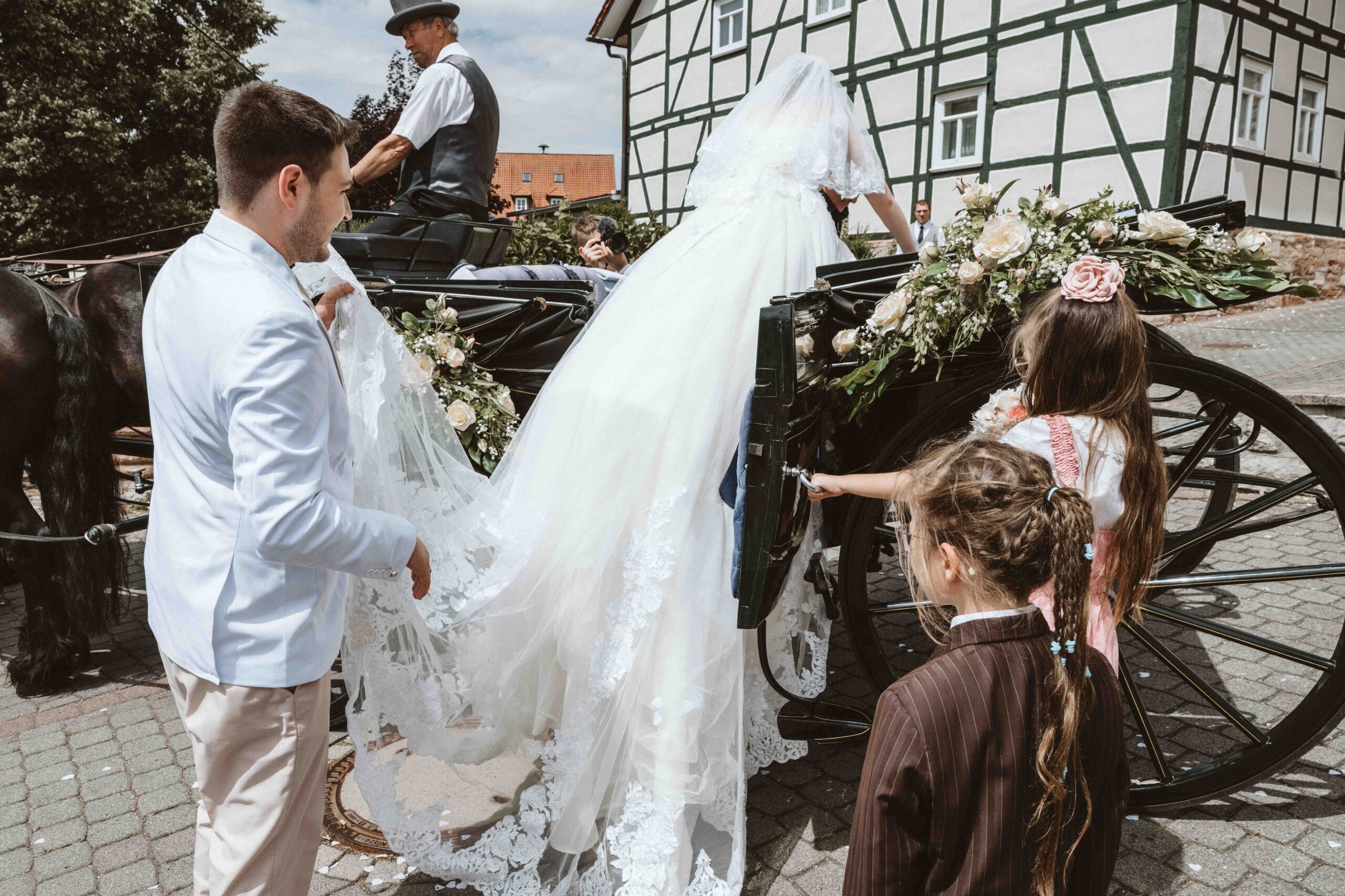 Der Bräutigam hilft der Braut mit dem langen Schleier, beim einsteigen in die Hochzeitskutsche
