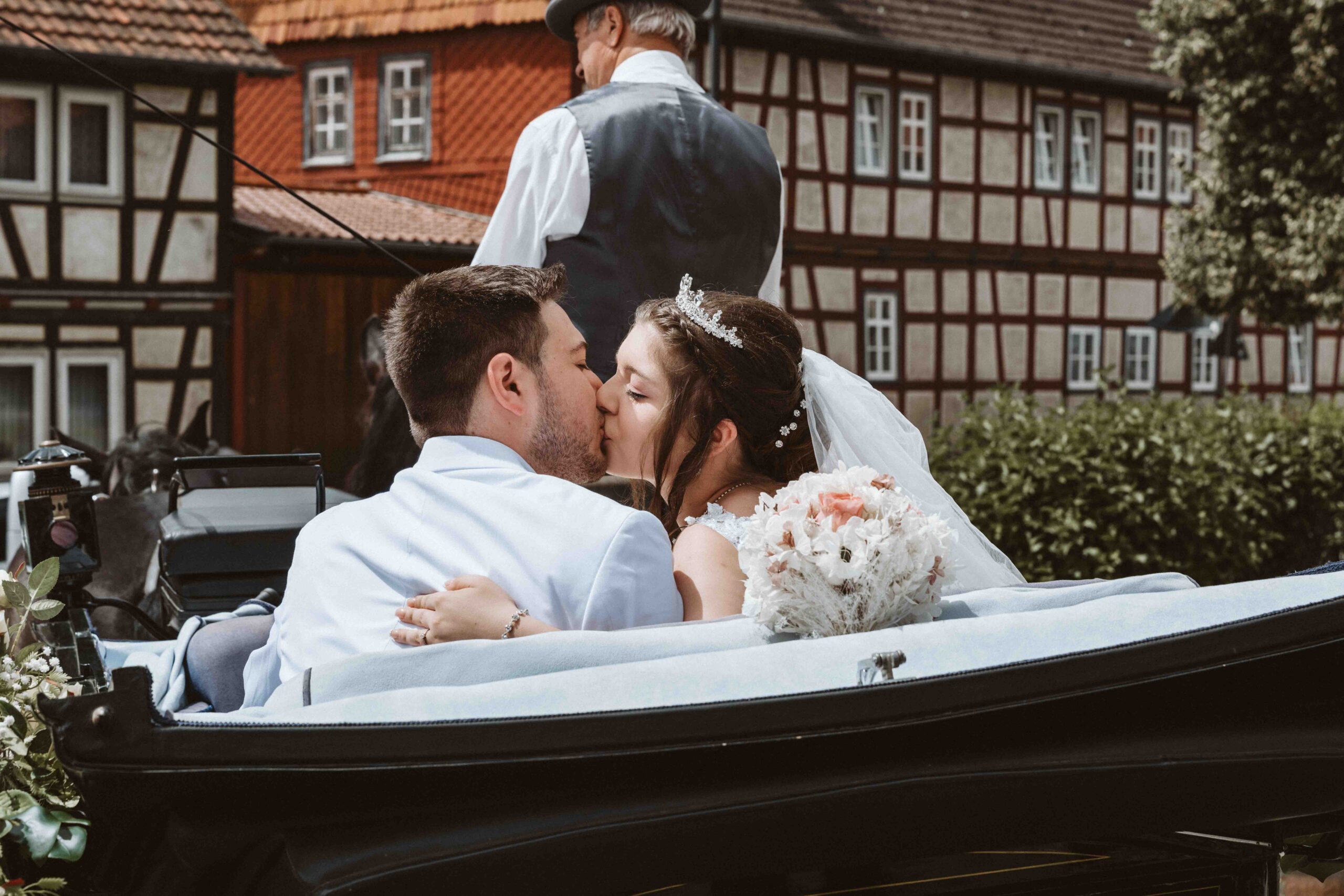 Das Brautpaar küsst sich in der wegfahrenden Hochzeitskutsche