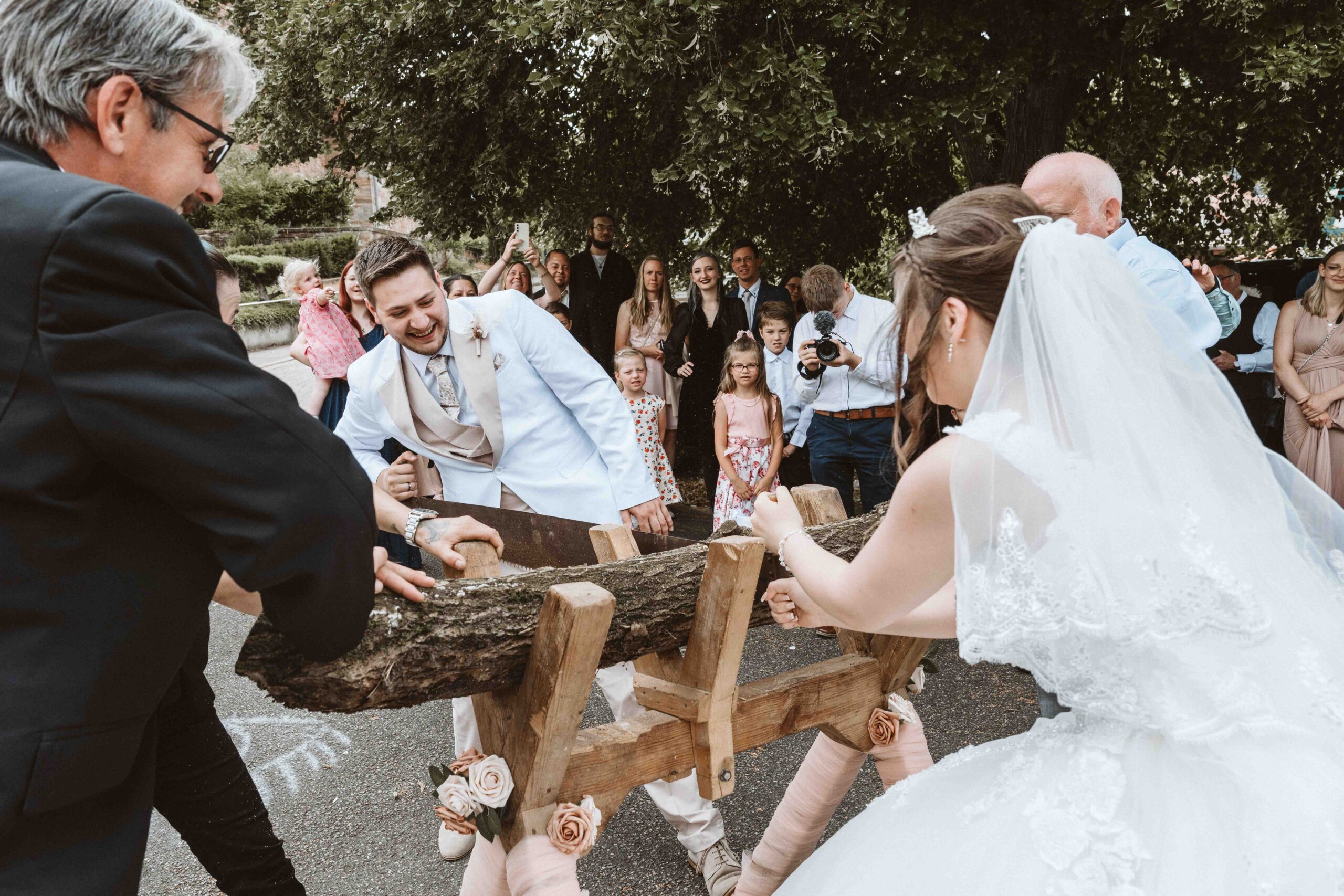 Hochzeitsfotografie, das Brautpaar beim durchsägen eines Baumstamm