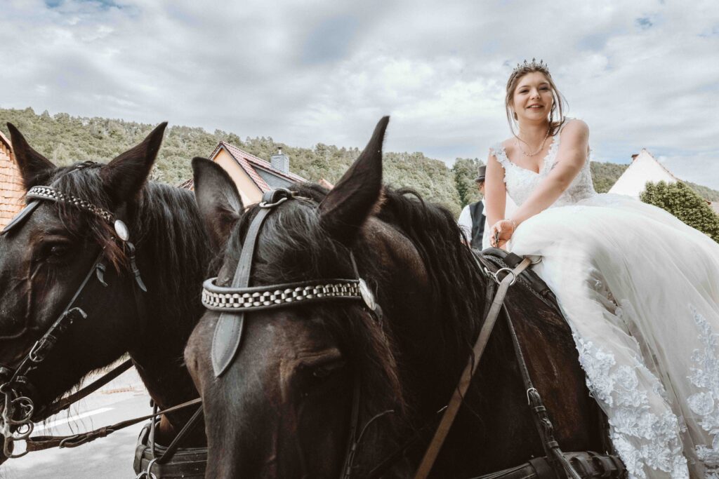 Die Braut sitzt mit Ihren Hochzeitskleid auf dem Kutschpferd