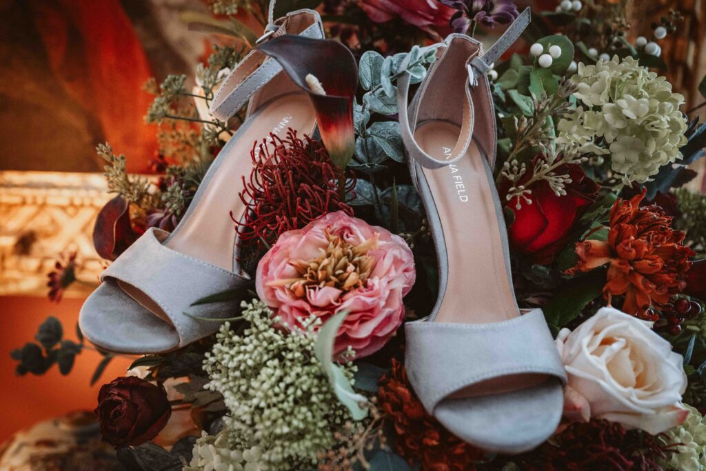 Graue Brautschuhe kunstvoll in einem Blumenstrauß während eines Editorial Styled Shootings arrangiert.