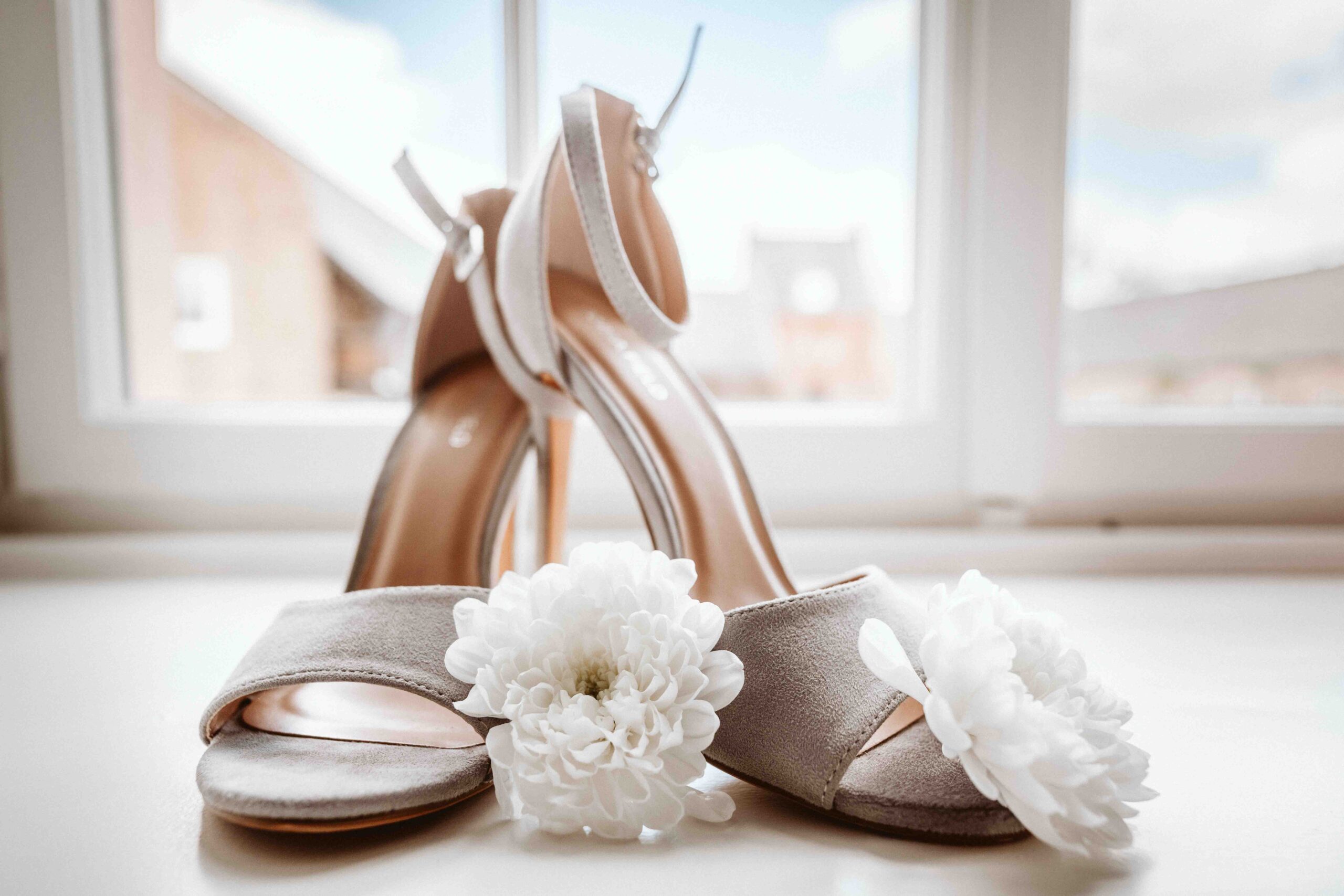 Elegante Brautschuhe mit weißen Blüten während des Getting Readys stilvoll fotografiert.