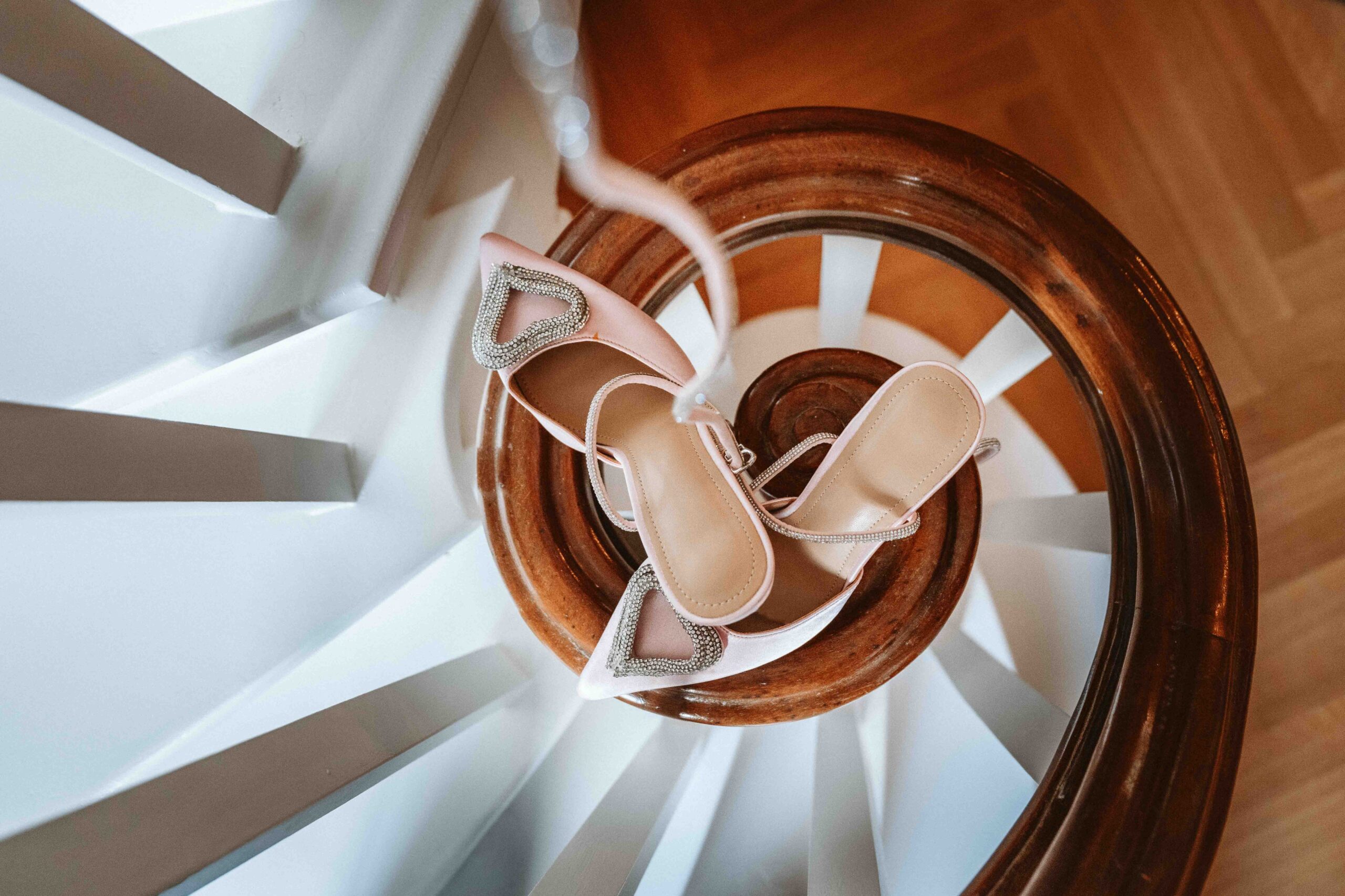 -Text
Rosafarbene Brautschuhe kunstvoll auf einer geschwungenen Holztreppe während des Getting Readys fotografiert.