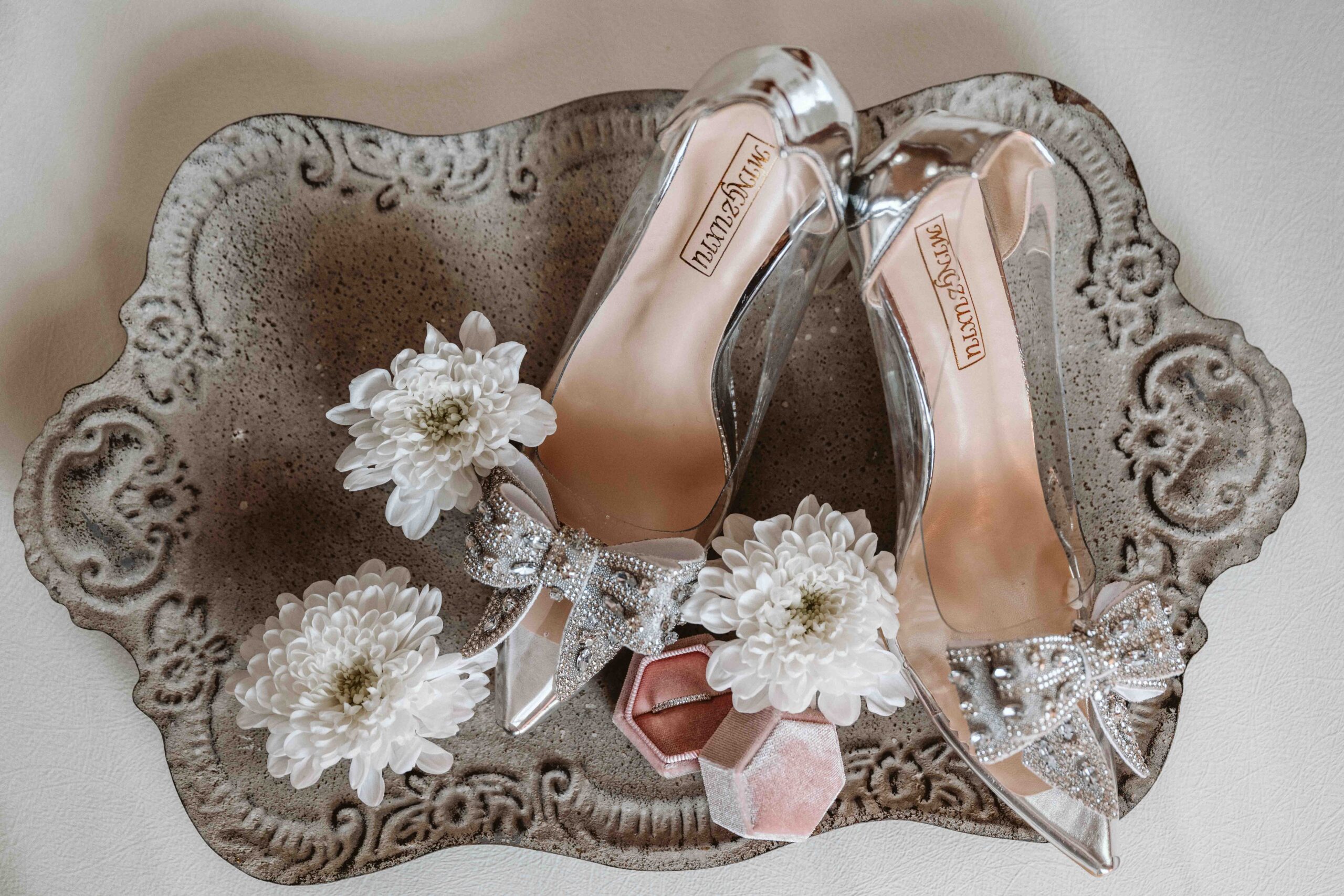 Elegante Brautschuhe mit Eheringen und weißen Blüten als stilvolle Detailaufnahme während des Getting Readys.