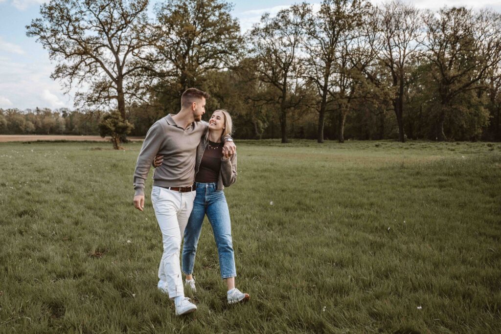 Paar läuft Arm in Arm während eines Engagementshootings durch eine sommerliche Landschaft.