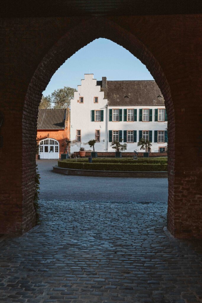 Blick durch das historische Tor von Schloss Burg Heimerzheim auf das elegante Hauptgebäude der Hochzeitslocation in NRW.