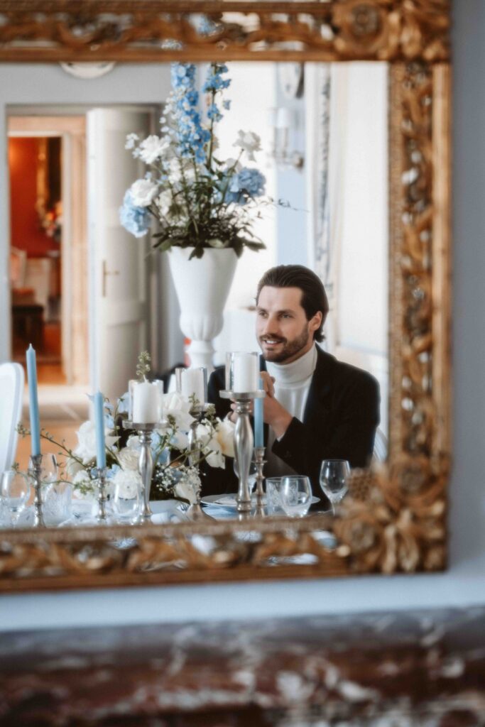 Spiegelaufnahme eines elegant gekleideten Bräutigams an einer festlich dekorierten Hochzeitstafel im historischen Ambiente von Schloss Burg Heimerzheim.