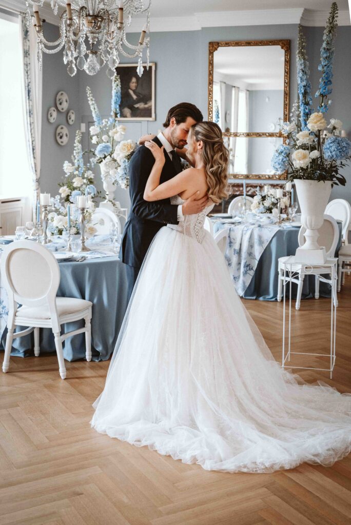 Braut und Bräutigam umarmen sich während ihres Paarshootings im festlich dekorierten Festsaal der Burg Heimerzheim zwischen elegant gedeckten Hochzeitstischen.