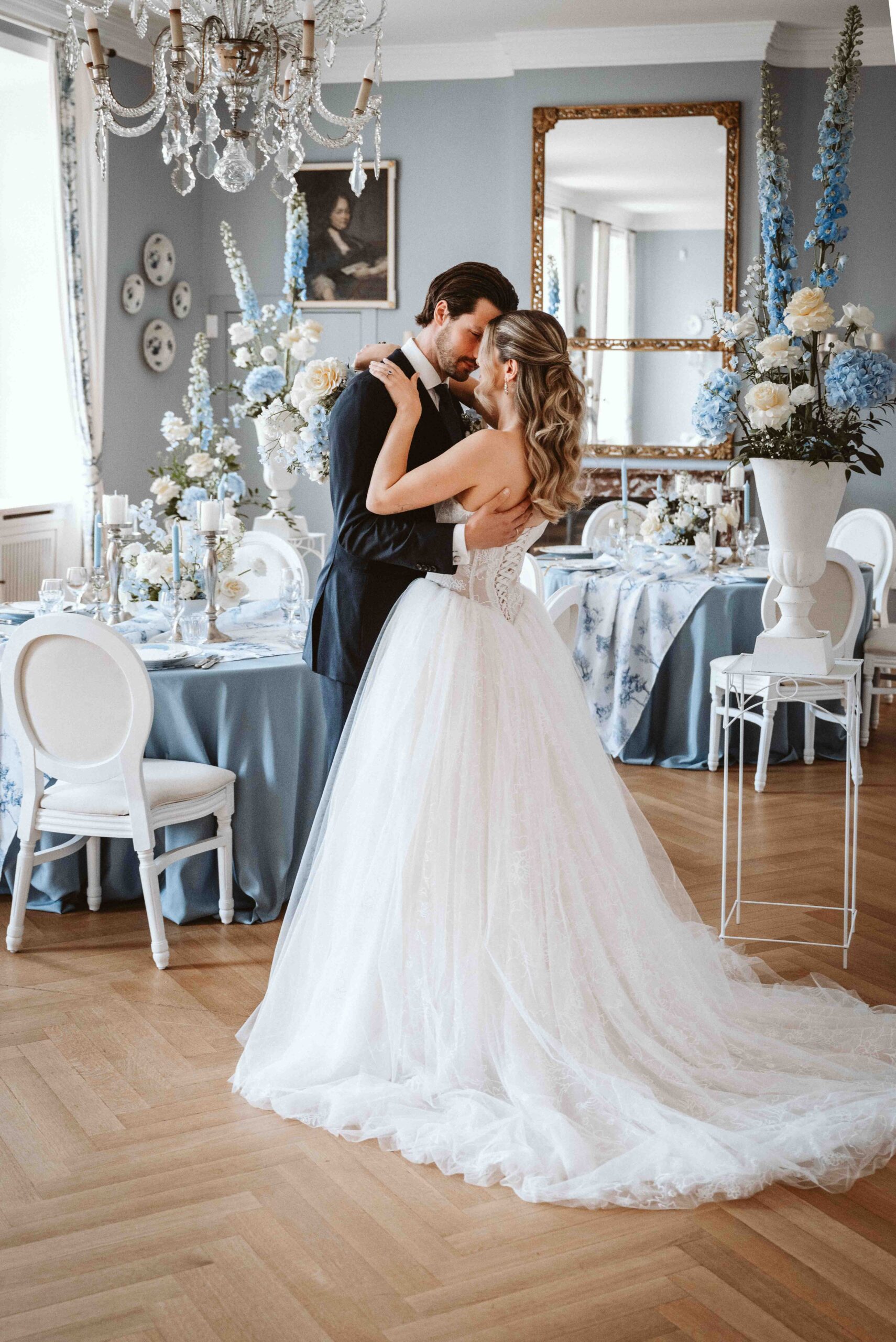 Braut und Bräutigam umarmen sich während ihres Paarshootings im festlich dekorierten Festsaal der Burg Heimerzheim zwischen elegant gedeckten Hochzeitstischen.