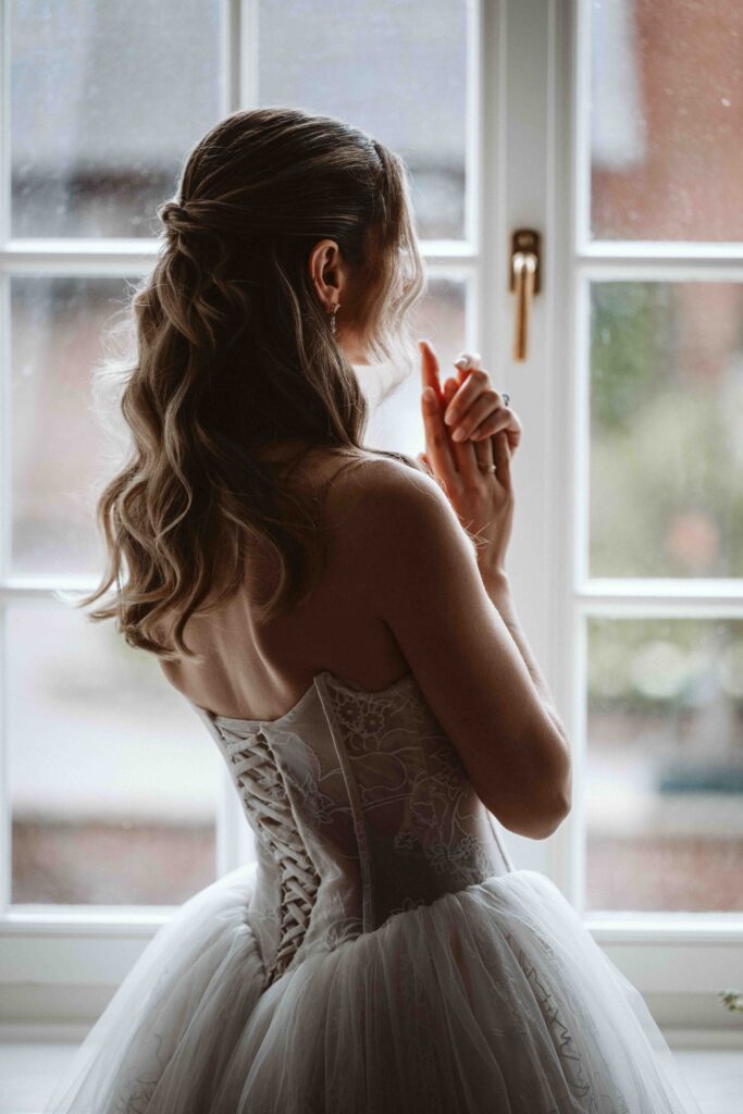 Braut blickt kurz vor ihrer Hochzeit aus einem historischen Fenster auf Burg Heimerzheim und genießt einen ruhigen Moment der Vorfreude.