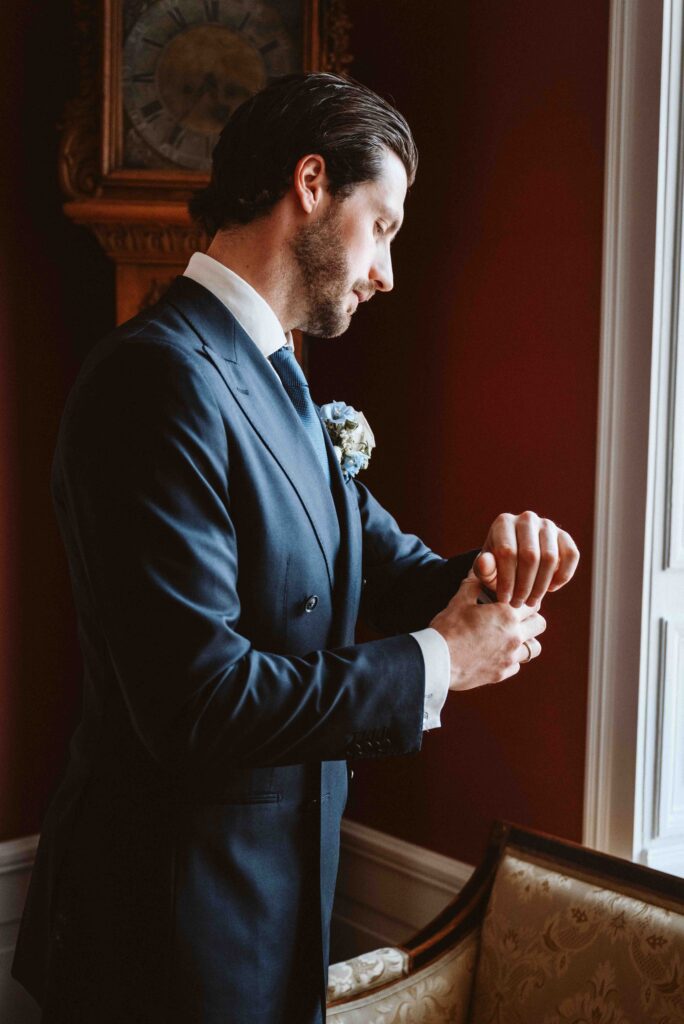 Elegantes Portrait eines Bräutigams am Fenster beim Anlegen seiner Manschette im historischen Ambiente von Schloss Burg Heimerzheim.