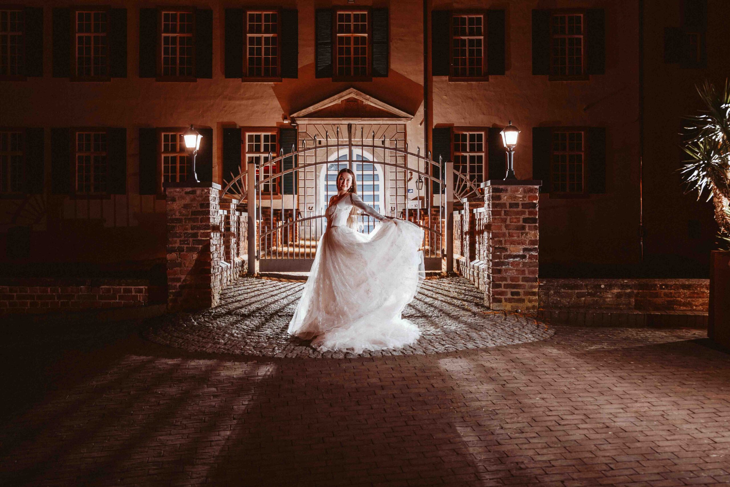 Braut hält ihr Kleid vor dem beleuchteten Burgeingang während eines nächtlichen Hochzeitsshootings.