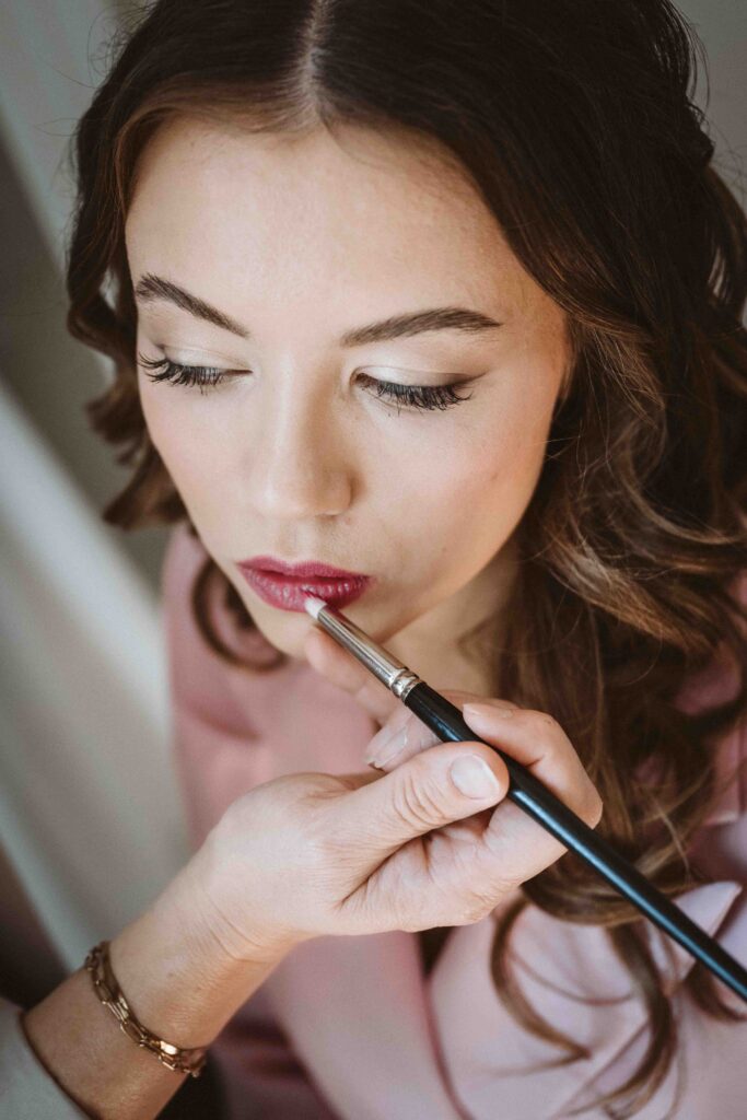 Detailaufnahme einer Braut während des Getting Ready, während die Visagistin den Lippenstift für die Hochzeit aufträgt.