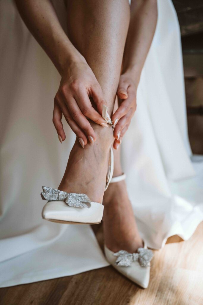 Braut schließt den Riemen ihrer Hochzeitsschuhe während des Getting Ready in der Villa Bodinus im Kölner Zoo.