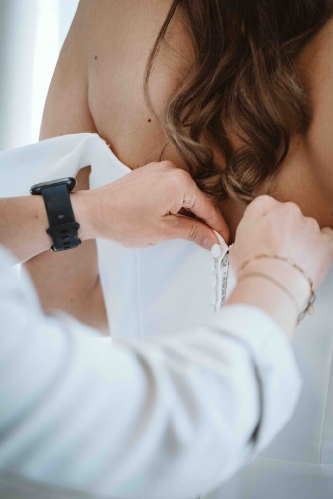 Detailaufnahme beim Ankleiden der Braut, während das Brautkleid kurz vor der Trauung geschlossen wird.