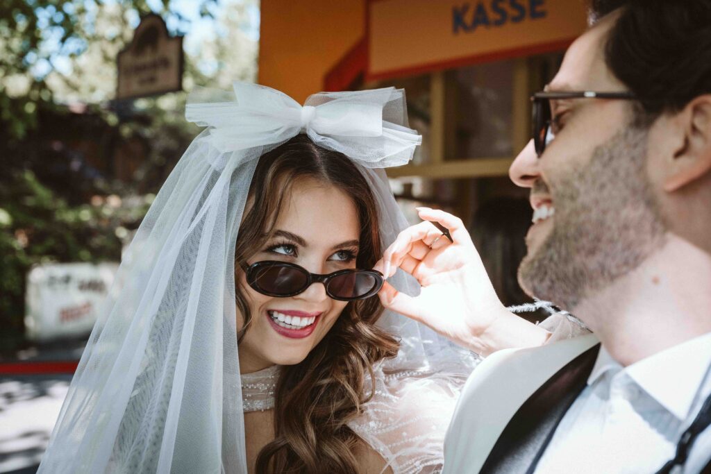 Braut blickt während eines Editorial Styled Shootings im Kölner Zoo über ihre Sonnenbrille zum Bräutigam.