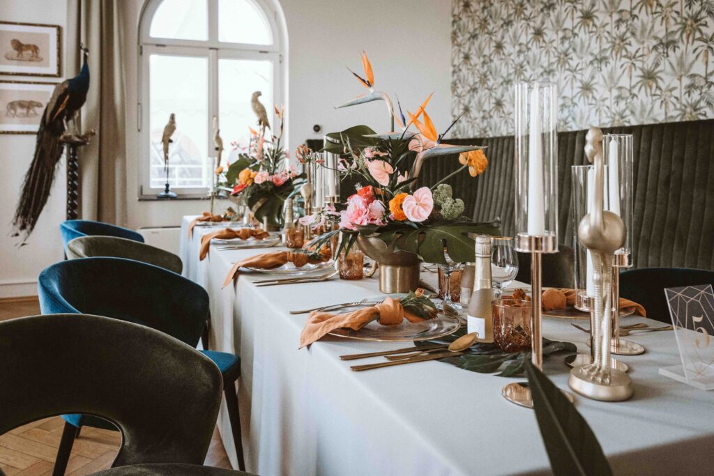 Stilvoll dekorierte Hochzeitstafel in der Villa Bodinus im Kölner Zoo mit tropischen Blumenarrangements, goldenen Kerzenhaltern, Samtstühlen und exotischem Interior Design