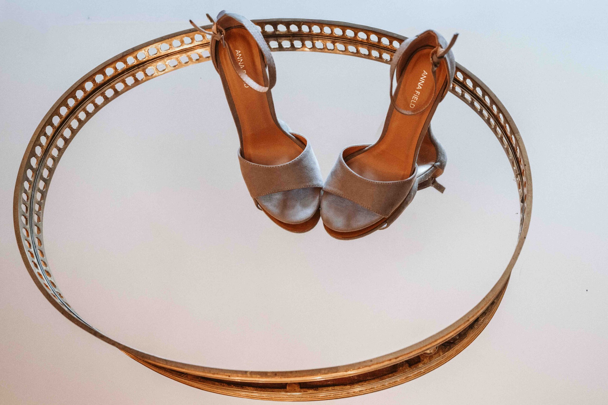 Elegante Brautschuhe auf einem goldenen Spiegel stilvoll während des Getting Readys fotografiert.