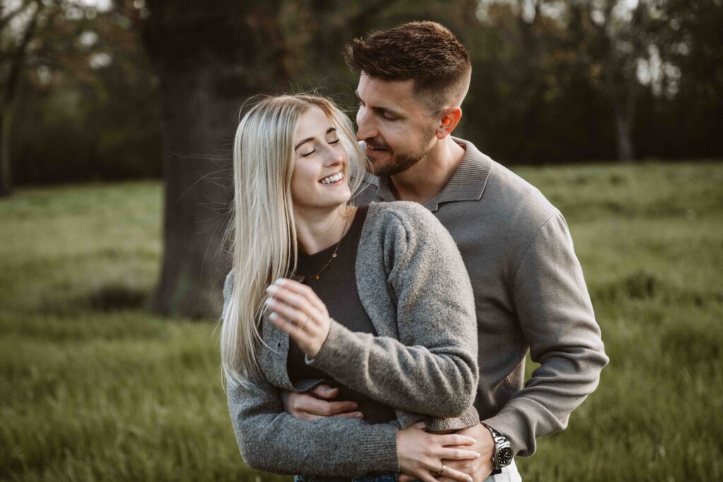 Verlobtes Paar umarmt sich während eines romantischen Engagement Shootings auf einer Wiese im warmen Abendlicht.