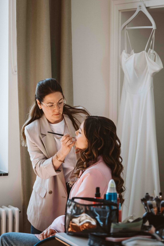 Visagistin trägt der Braut beim Getting Ready das letzte Make-up auf – Vorbereitungen vor der Hochzeit.