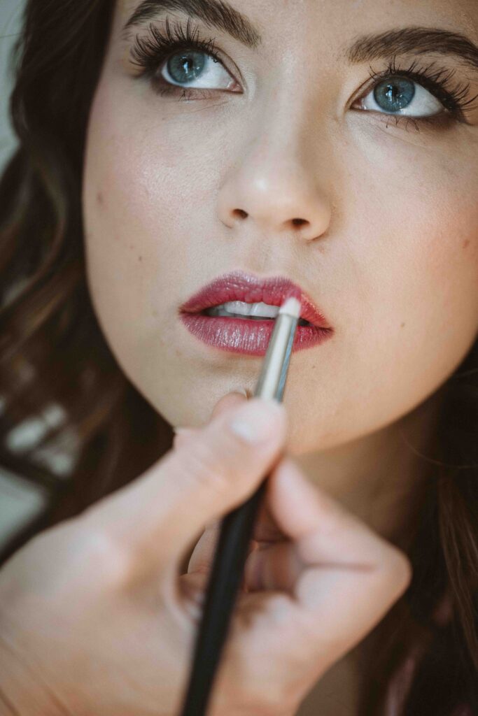 Nahaufnahme einer Visagistin beim Auftragen des Lippenstifts während des Brautstylings vor der Hochzeit.