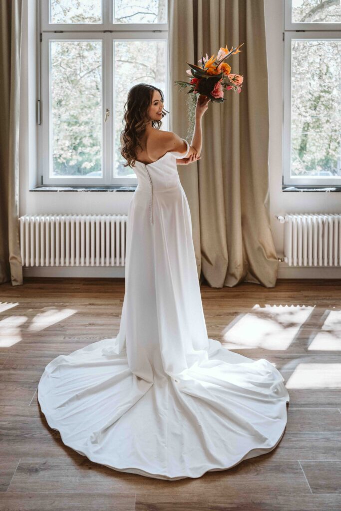 Braut hebt ihren Brautstrauß im natürlichen Tageslicht und genießt einen besonderen Moment während des Gettings Ready vor der Hochzeit.