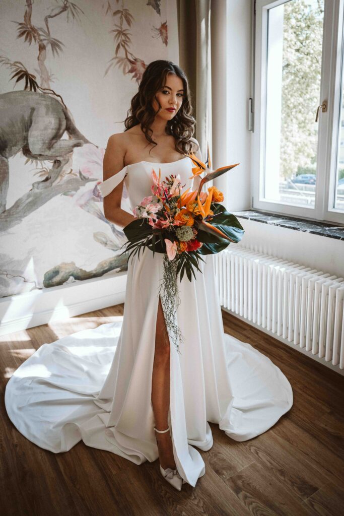 Braut mit farbenfrohem Brautstrauß im natürlichen Fensterlicht während des Gettings Ready vor der Hochzeit.