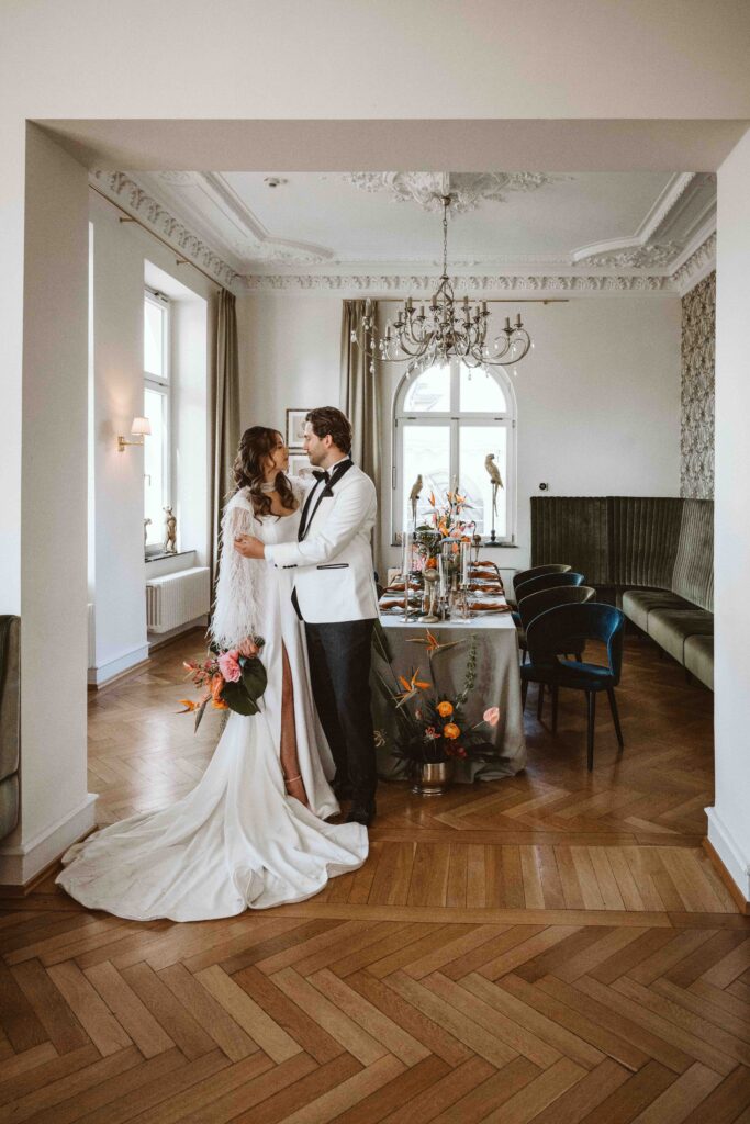 Braut und Bräutigam stehen während ihres Paarshootings im historischen Festsaal der Villa Bodinus vor einer festlich dekorierten Hochzeitstafel.