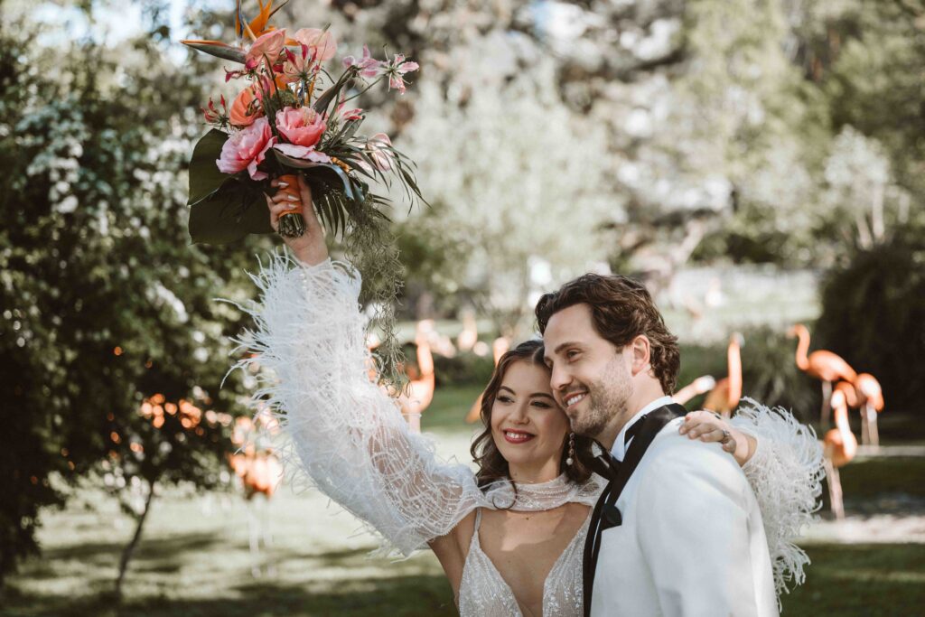 Braut hebt ihren Brautstrauß vor Flamingos beim Styled Wedding Shooting im Kölner Zoo